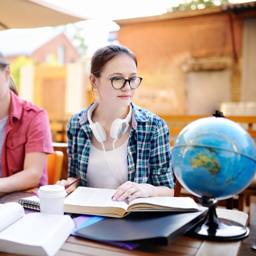 A youth seated at a table with a textbook looks at a nearby globe