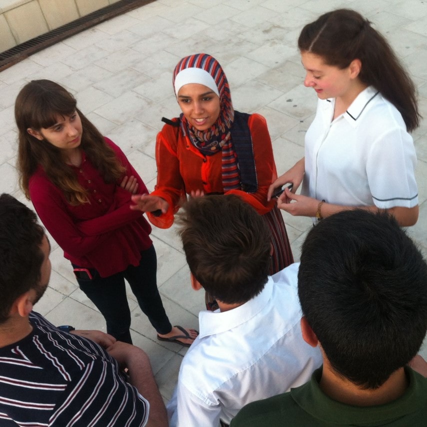 A person in a headscarf addresses a group of students in a courtyard