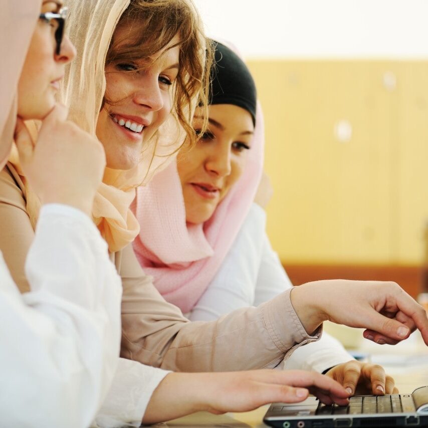 Three youths in headscarves use a laptop computer