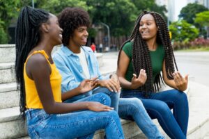 Three dark-skinned youths sit at an outdoor fountain talking and smiling