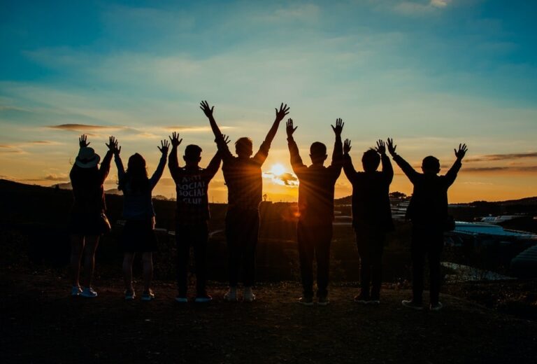 Seven youths raise their hands in unison before a sunset