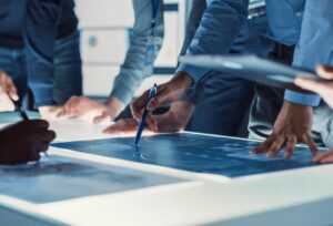 Several hands point to architectural blueprints sit on a lighted table