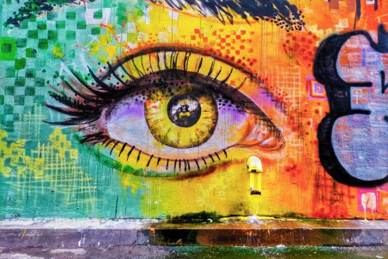 A mural painting of an eye in the center with rainbow colors around it. Purple graffiti art on the right side