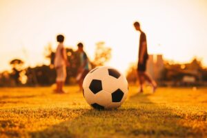 A soccer ball in the middle of a pitch with several players in the background