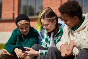 Four youths in coats sit outside a school looking at a mobile phone