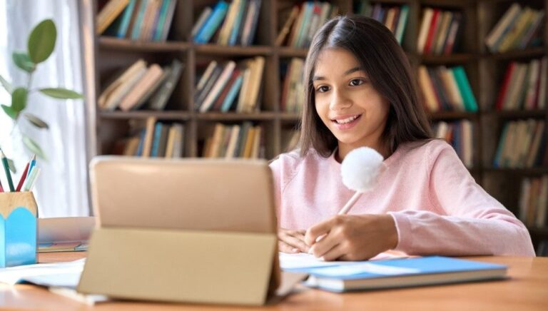 A youth seated at a library table smiles into an iPad