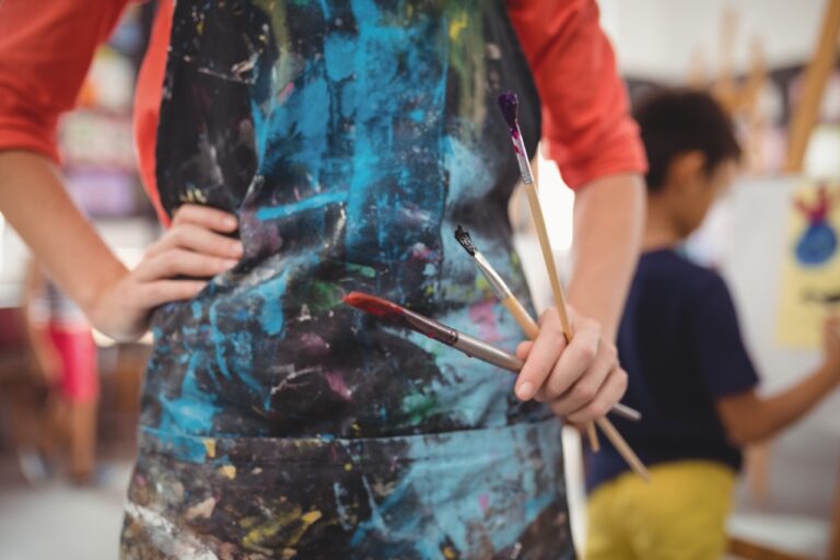 An artist with a paint-spattered smock, holding paintbrushes