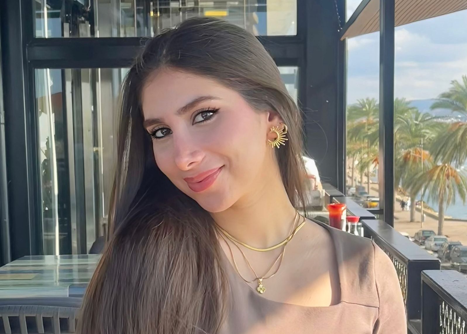 Picture of young girl with olive skin, wearing a light brown top in front of a window