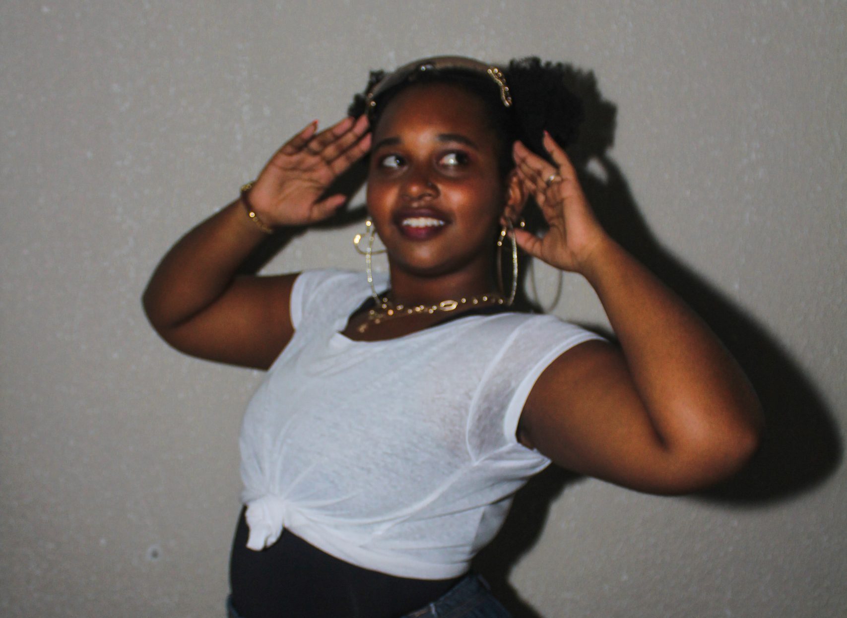Girl with dark skin and ponytails posing in front of a white wall