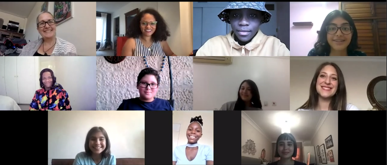 A grid of eleven video call windows showing a diverse group of people of various ages and backgrounds. Most individuals are smiling and looking at their cameras from various indoor settings. Some participants are wearing glasses, one is wearing a patterned bucket hat, and another is wearing a vibrant, multicolored jacket.